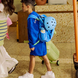 Child in blue outfit with sky blue helmet and backpack walking in a room with tiled floor and furniture.