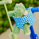 Green plush toy with a blue/green gingham doll carrier attached to a blue skootcase outdoors