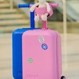 Pink and blue children's skootcases with a unicorn toy on top inside the pink gingham skoot doll carrier, set against an airport background.
