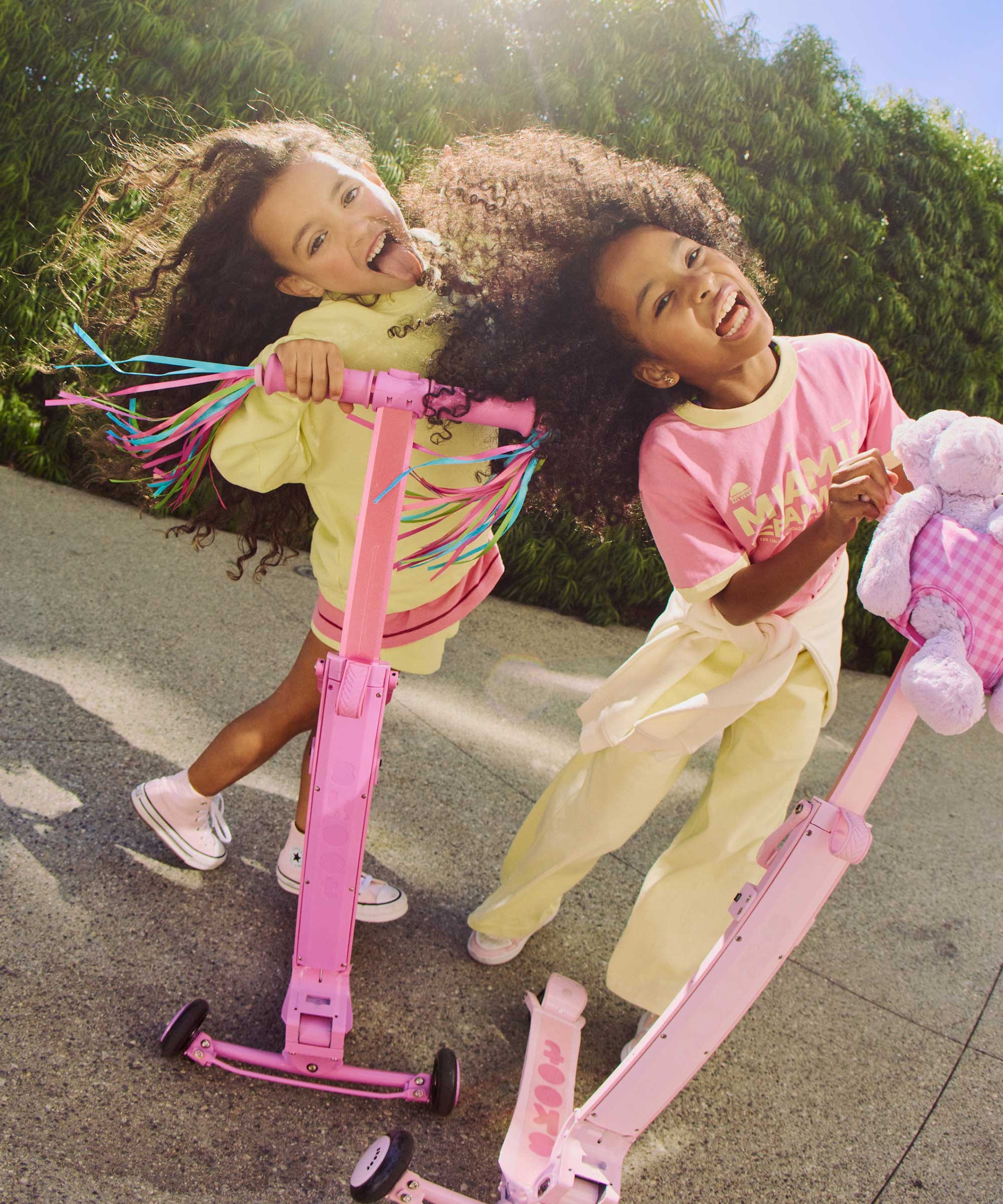 Two children playing with pink skoot skootcases on a sunny day.